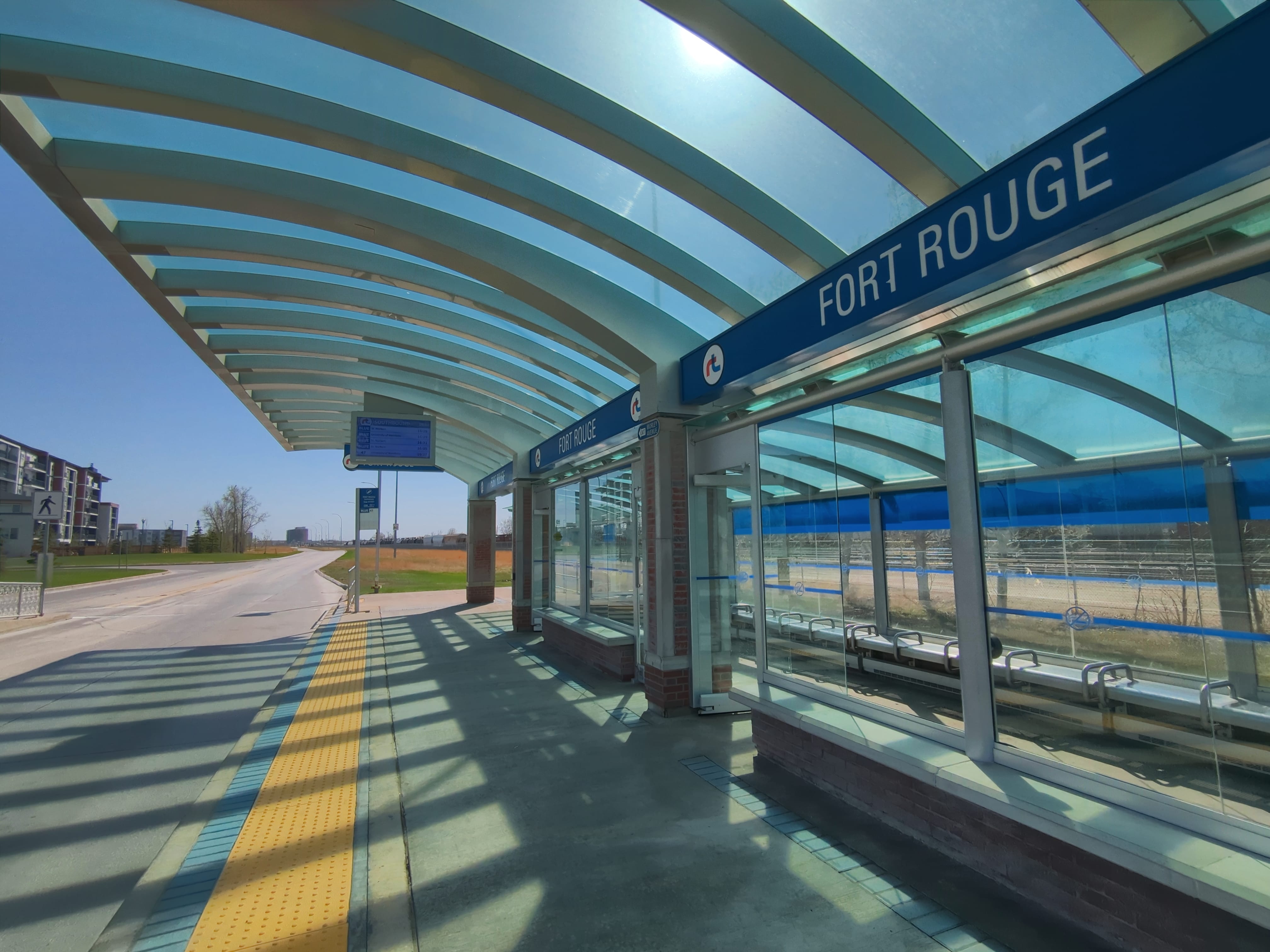 Under Fort Rogue Station's glass shelter, with digital signage displaying times