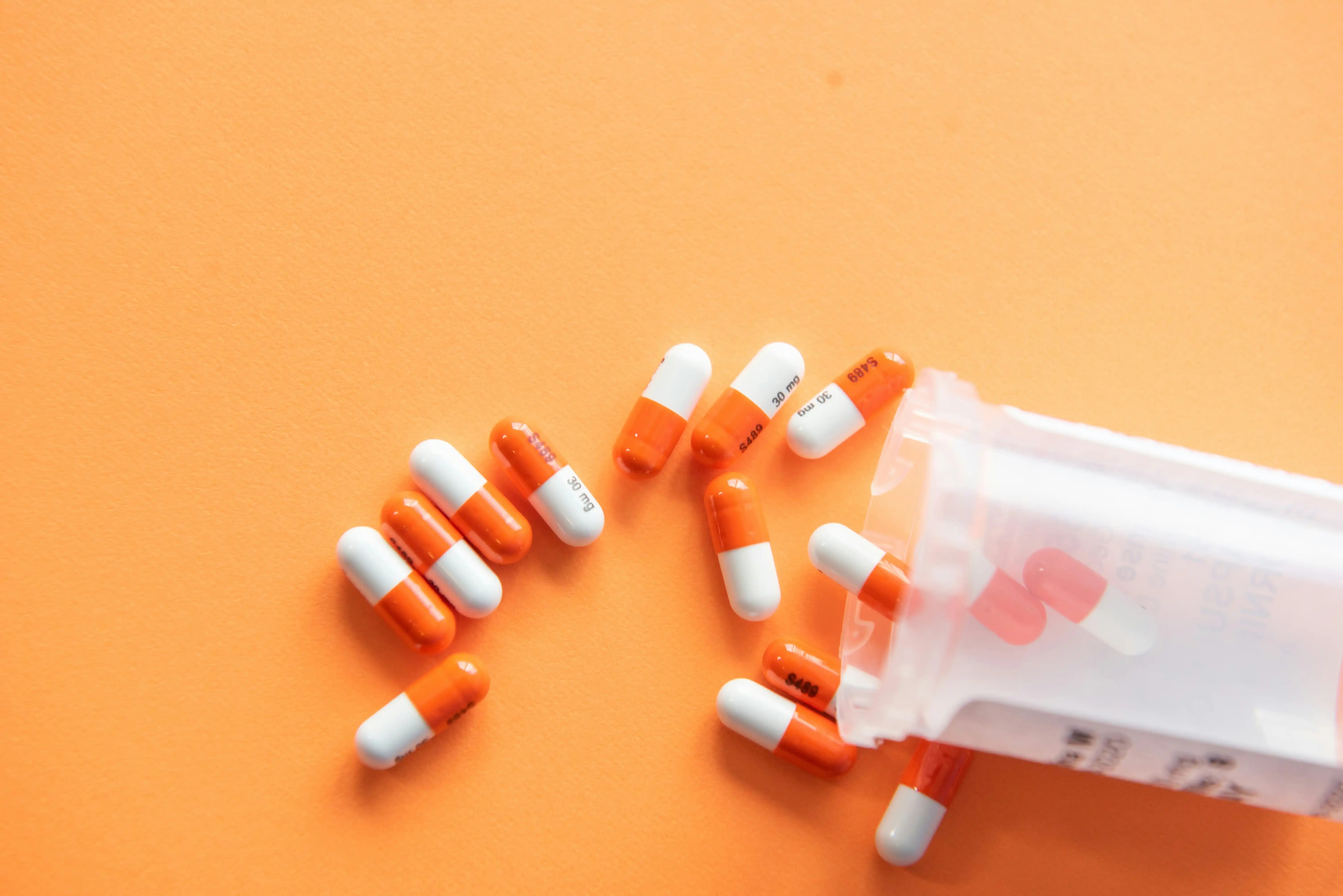 White and orange prescription pills carefully spilled, with its bottle.